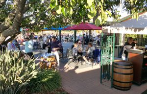 A wine tasting event, showing people sitting under colorful umbrellas near wine barrels